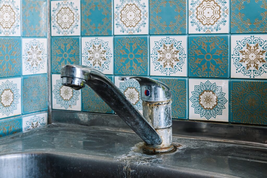 Old rusty sink faucet in kitchen. Rust streaks, calcium scale, hard water.